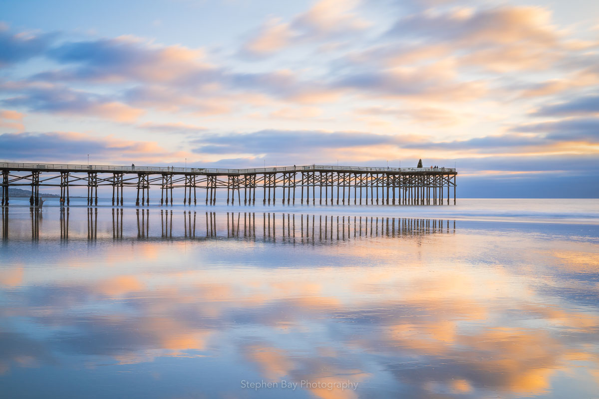 Crystal Pier in Pacific Beach during a low tide. The sand has a thin layer of water covering it and acts like a mirror and reflects the clouds.