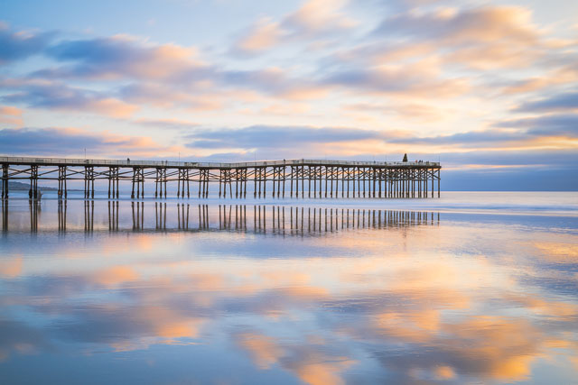 Crystal Pier in Pacific Beach during a low tide. The sand has a thin layer of water covering it and acts like a mirror and reflects the clouds.