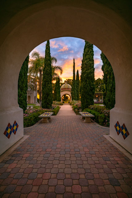 Pathway in Balboa Park leading into a colorful sunset. The pathway is framed by an arch.