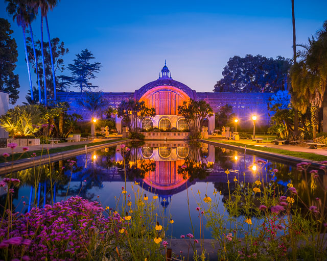 Botanical Building and lily pond in the early morning hours. There are flowers in the foreground and a reflection of the botanical building in the water.