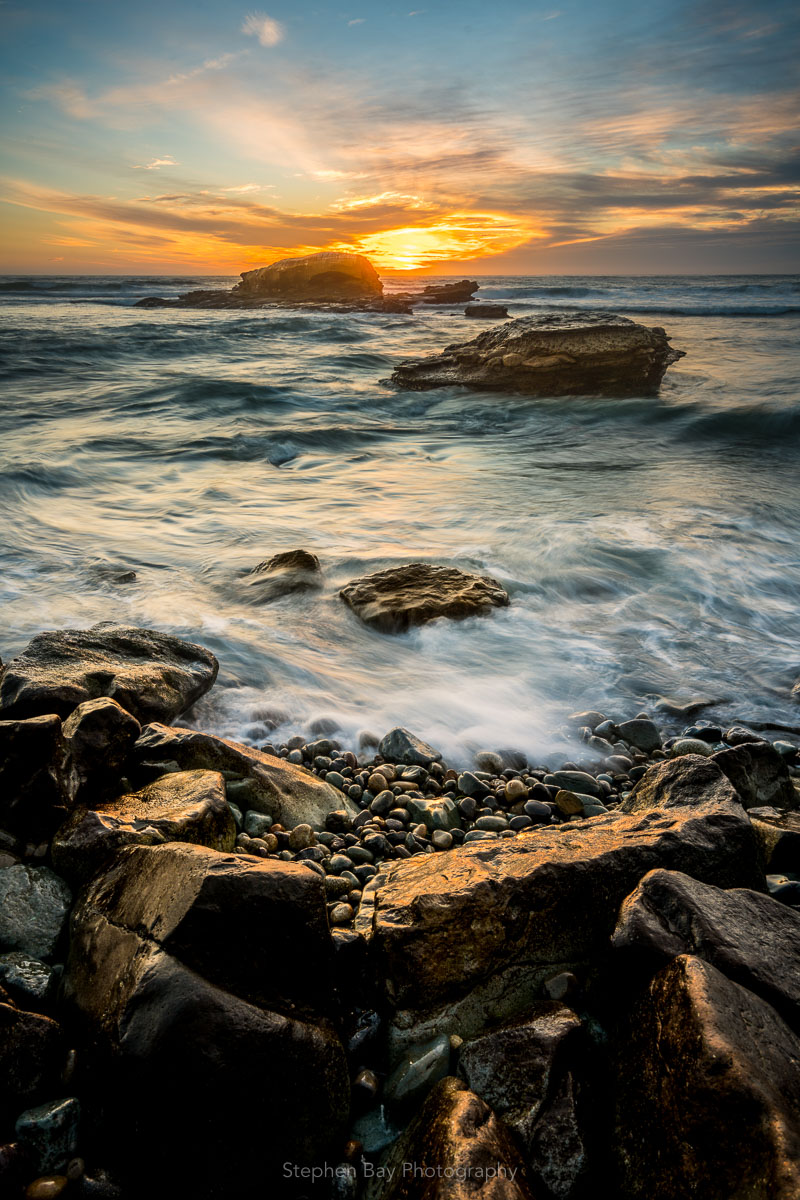 Sunset at Bird Rock in La Jolla. Bird rock is in the distance and at the viewers feet are wet rocks glistening in the sunlight.