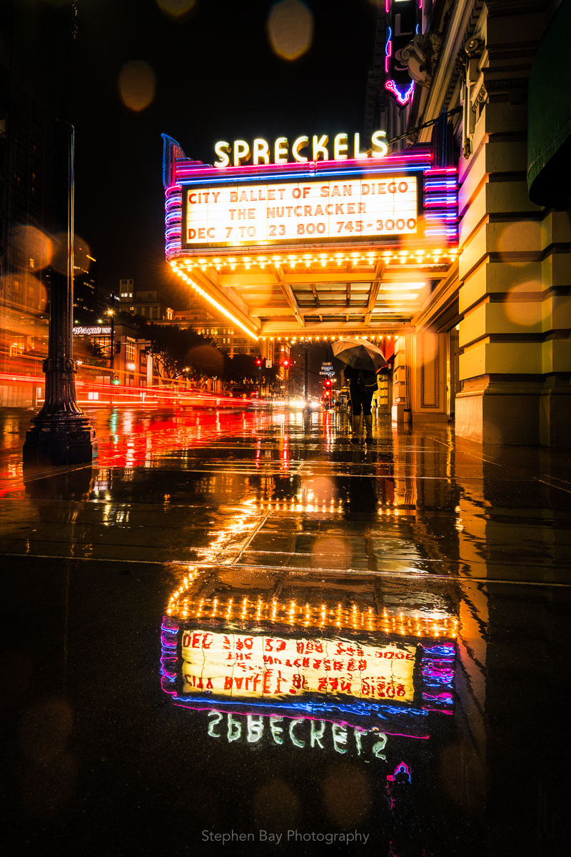 Spreckels theatre in the rain at night. There is a reflection of the theatre sign in the water pooling on the sidewalk.