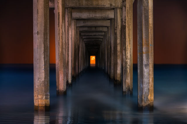 Vew of Scripps pier from between the support pylons. The moon is setting and can be seen aligned in the center of the opening.