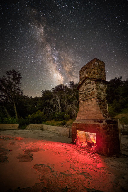 The remains of an abandoned building with just a chimney remaining under the night sky.