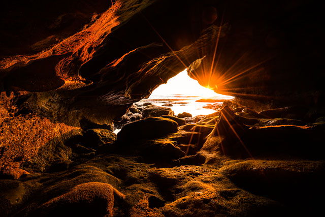 Rum runner’s cave in Sunset Cliffs. The photo is taken at sunset and light is streaming into the cave an illuminate the cave walls.