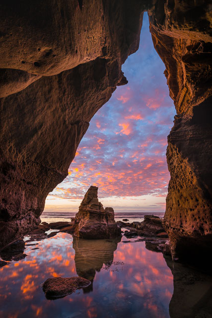 Sea cave hidden in the bluffs at Sunset Cliffs, San Diego. An amazing sunset is seen from the inside and is reflected into the water at the cave entrance.